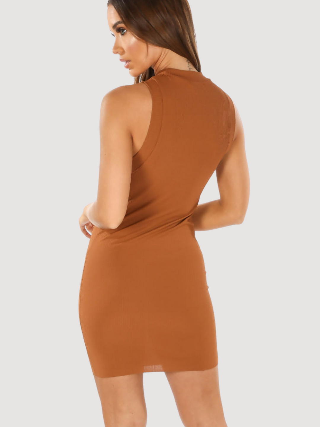 Model wears a brown sleeveless ribbed mini dress in front of a plain light grey background. The model has tanned skin and brown hair, she stands with the back to the camera and looks to the side, the racer back design of the dress can be seen.