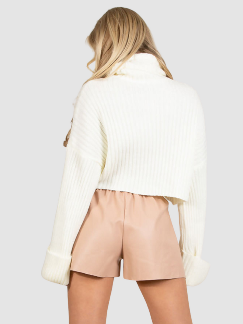 Model stands in front of a plain background, she stands with her back to the  camera , and wears a rose coloured faux leather paper bag shorts. The back of the shorts can be seen. 