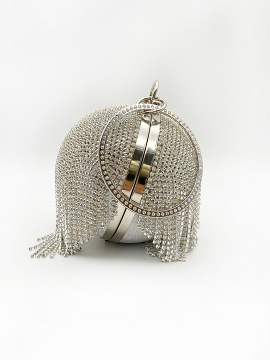 Silver bag, with diamante tassels, clasp fastening and a round diamante handle. The picture shows the bag photographed from the side, demonstrating the sequin diamante tassel, with the rounded handle visible also. 