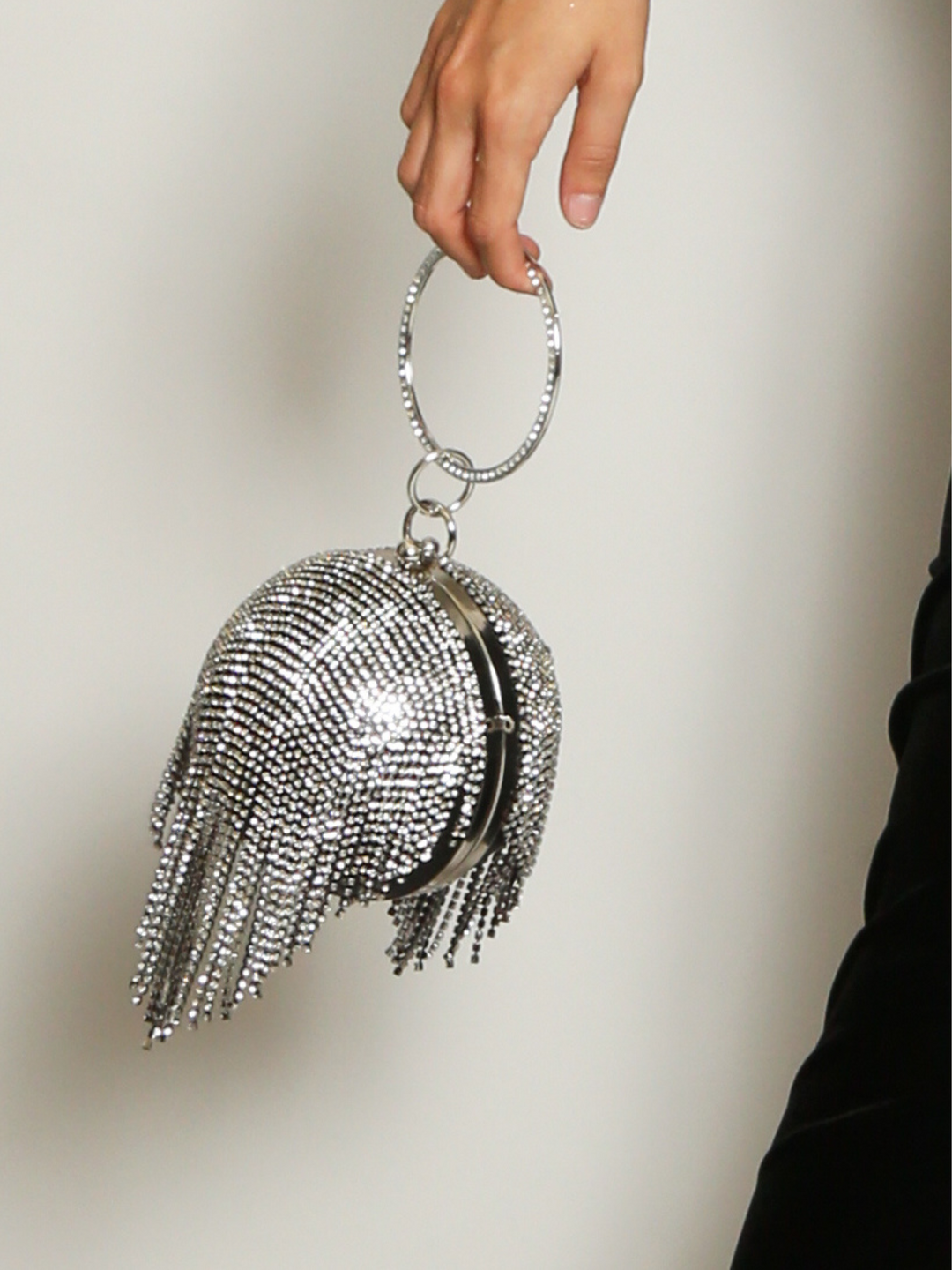 Silver bag, with diamante tassels, clasp fastening and a round dianante handle. Model holds the handle by its round handle, the tasseled diamantes can be seen. 