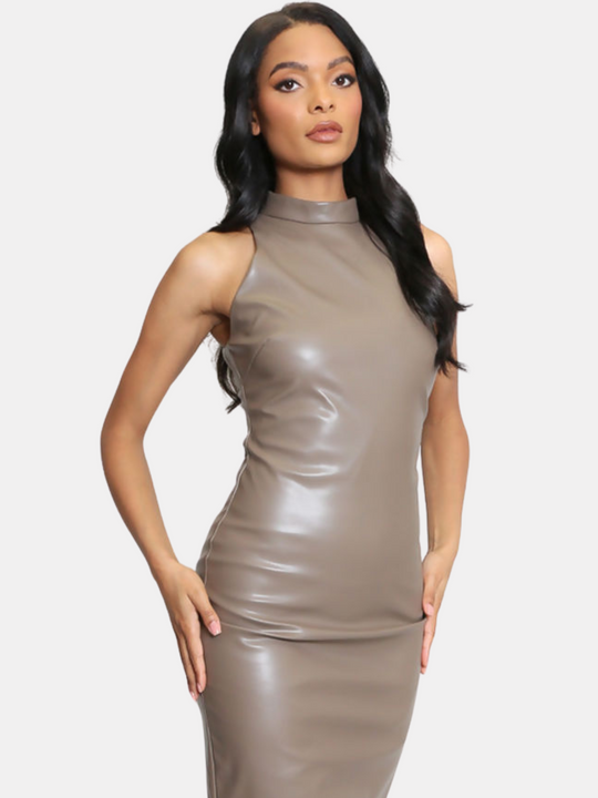Female model stands in front of a light taupe plain background. The model wears a taupe faux leather midi dress, with a high neck and sleeveless design. The model has light model stands with her hips brown skin and long black hair, she places her hands by her sides. 