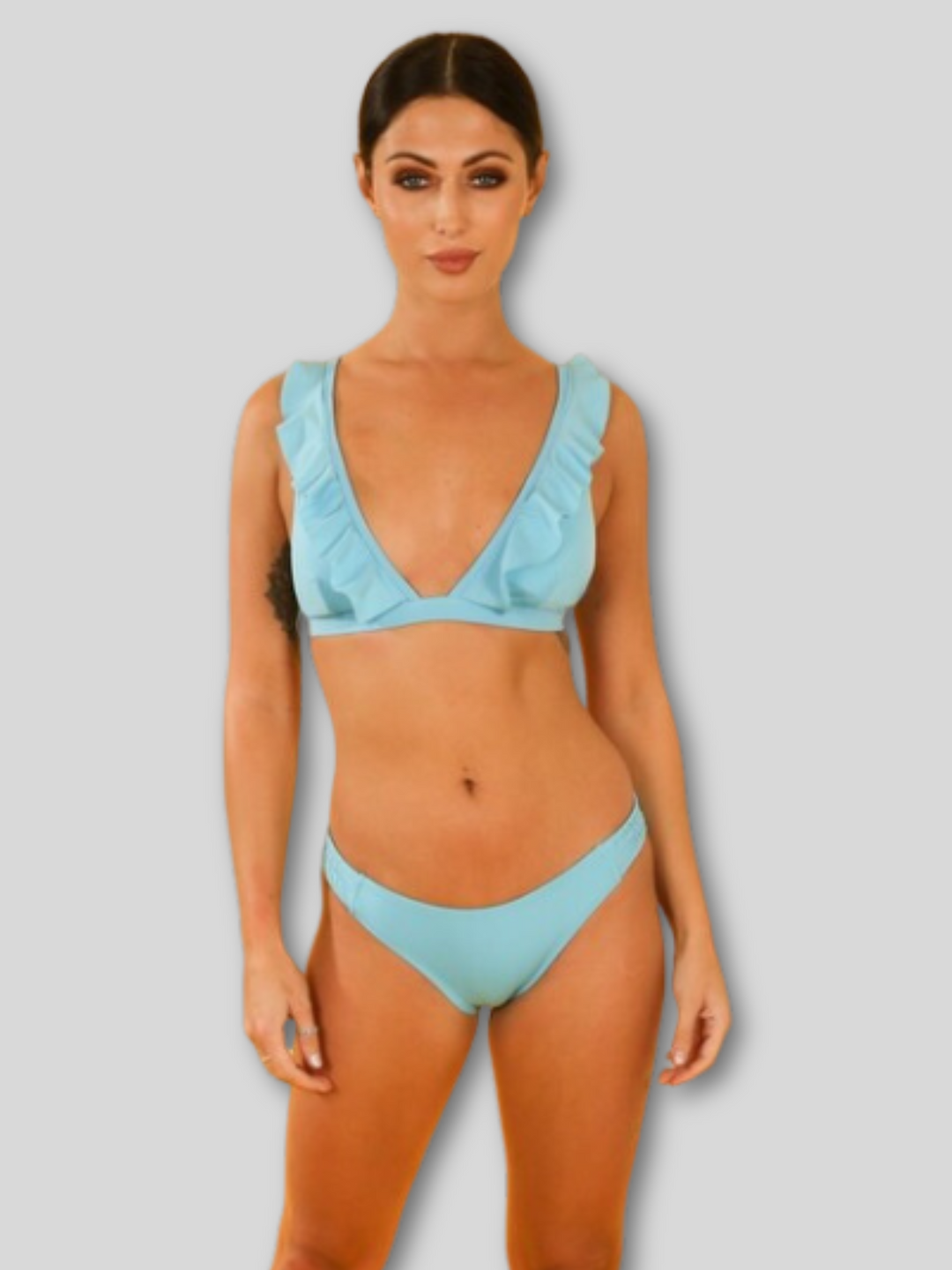 Model wears a turquoise bikiniset with padded bikini cup detailing and a frill trim. Model stands with her hands by her sides.