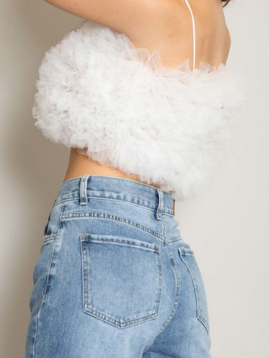 Model wears  a white organza ruffled crop top ,with spaghetti strap and zip back fastening. Model stands to the side, the side of the organza top and the spaghetti straps can be seen. 