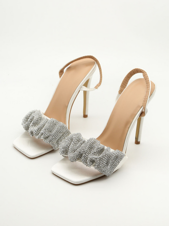 Satin high heeled shoe with open toe front, sling back strap and a diamante front. The diamante heel is in front of a white background. 