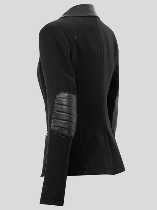 Ghost mannequin stands in front of a grey background. The ghost mannequin wears a  single breasted black tailored blazer, with faux leather lapel and single front button fasten. The ghost mannequin stands to the side, the in front of the blazer, faux leather cuff elbows can be seen.