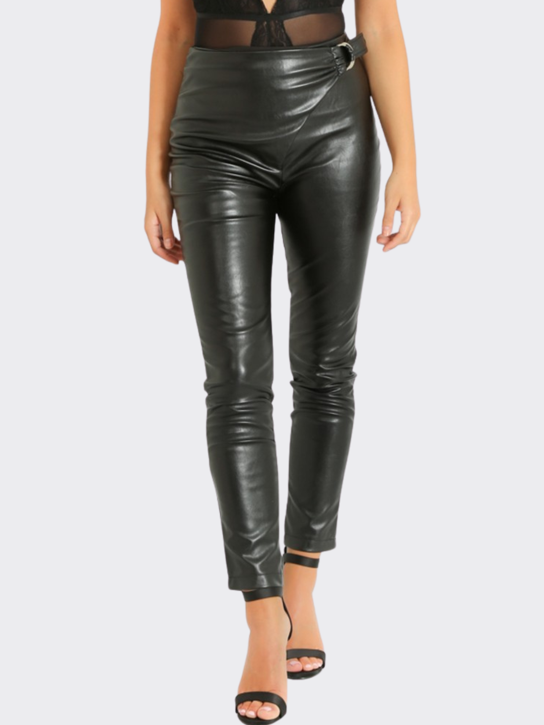 Female model stands in front of a blank background, she wears a faux leather trousers with wrap front design, with d buckle fastening, the front of the trousers can be seen. 