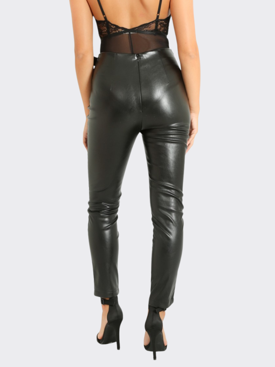 Female model stands in front of a blank background, she wears a faux leather trousers with wrap front design, with d buckle fastening, the model stands with her back to the camera, the back of the trousers can be seen, including the invisible zip back fastening.