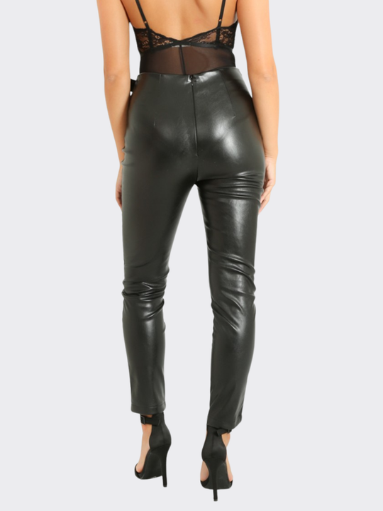 Female model stands in front of a blank background, she wears a faux leather trousers with wrap front design, with d buckle fastening, the model stands with her back to the camera, the back of the trousers can be seen, including the invisible zip back fastening.