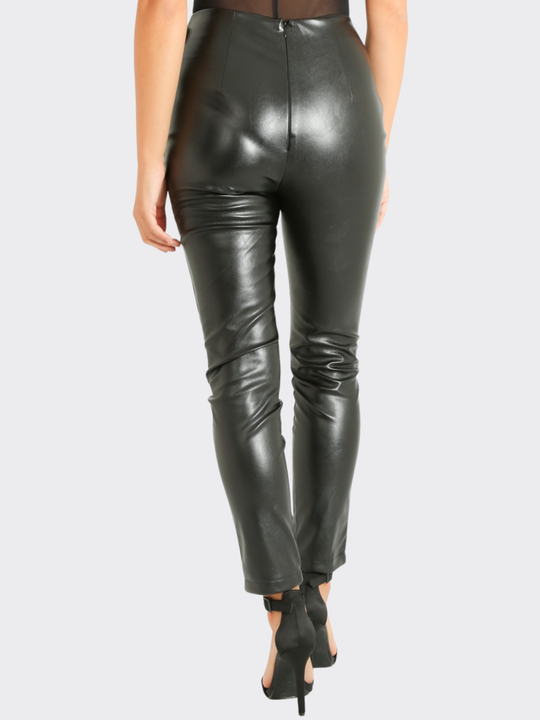 Female model stands in front of a blank background, she wears a faux leather trousers with wrap front design, with d buckle fastening, the model stands with her back to the camera, the back of the trousers can be seen, including the invisible zip back fastening. The model stands with one feet slightly in front of the other. 