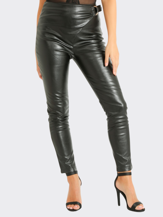 Female model stands in front of a blank background, she wears a faux leather trousers with wrap front design, with d buckle fastening. The model wears black stiletto shoe, she places one hand on her hip and the other behind her back. 