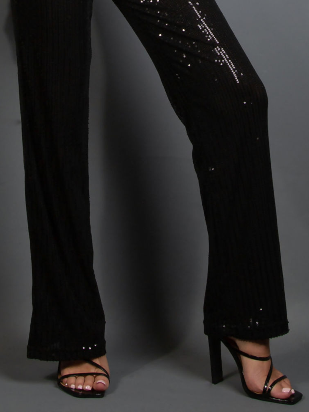 Black sequin pants worn by a model on a gray background. The bottom of the sequinned trousers can be seen, including the trousers wide fitting. 