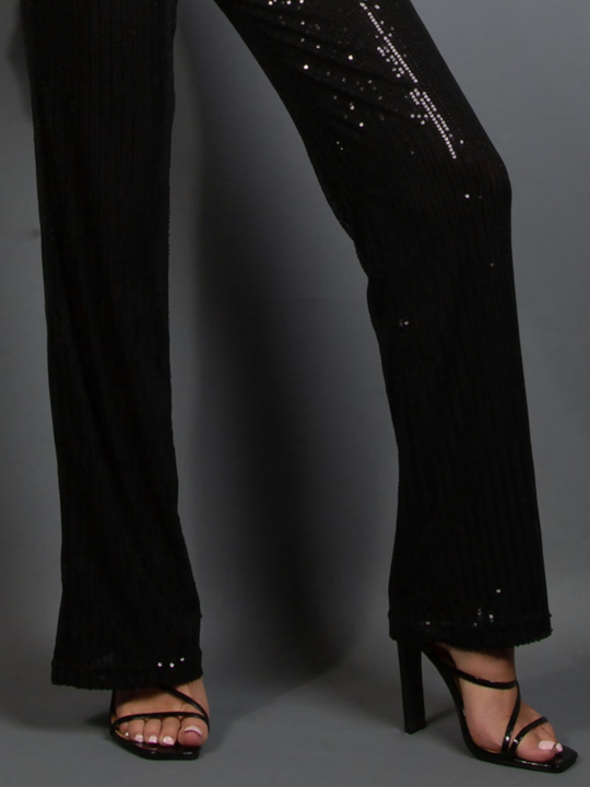 Black sequin pants worn by a model on a gray background. The bottom of the sequinned trousers can be seen, including the trousers wide fitting. 