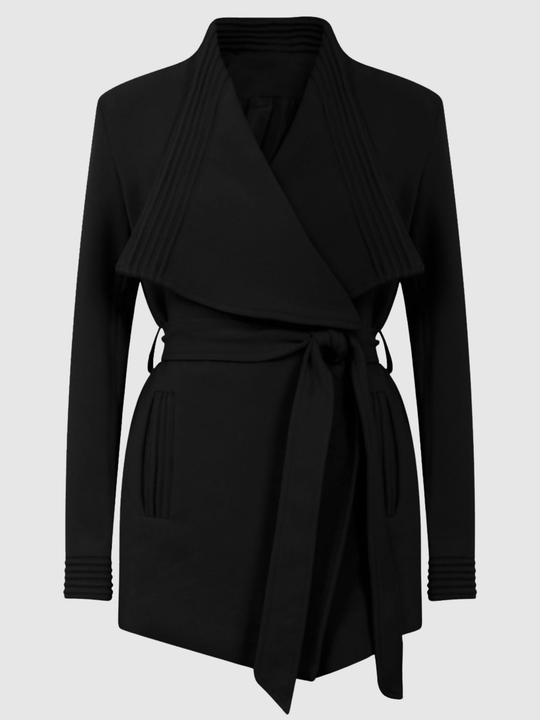 Ghost mannequin stands in front of a plain light grey background. The ghost mannequin  faces forward and wears of a black wrap coat, with a belted waist fastening. The coat has long sleeves.