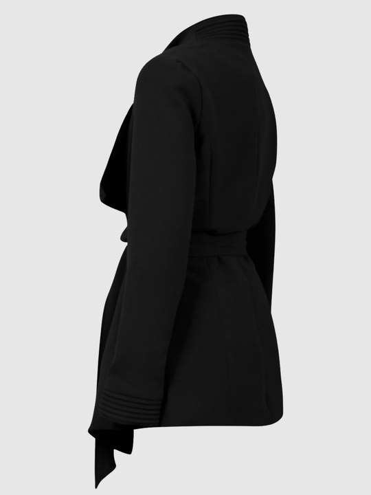 Ghost mannequin stands in front of a plain light grey background. The ghost mannequin  wears a black wrap coat, with a belted waist fastening, the coat has long sleeves. The ghost mannequin stands to the side, the side of the coat and the back can be seen. 