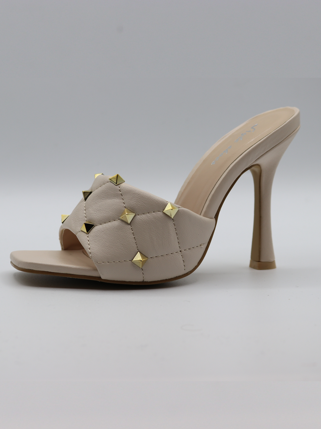 Cream quilted faux leather mule heels with gold studded heels. Photo shows the shoes from the side against a white backdrop.