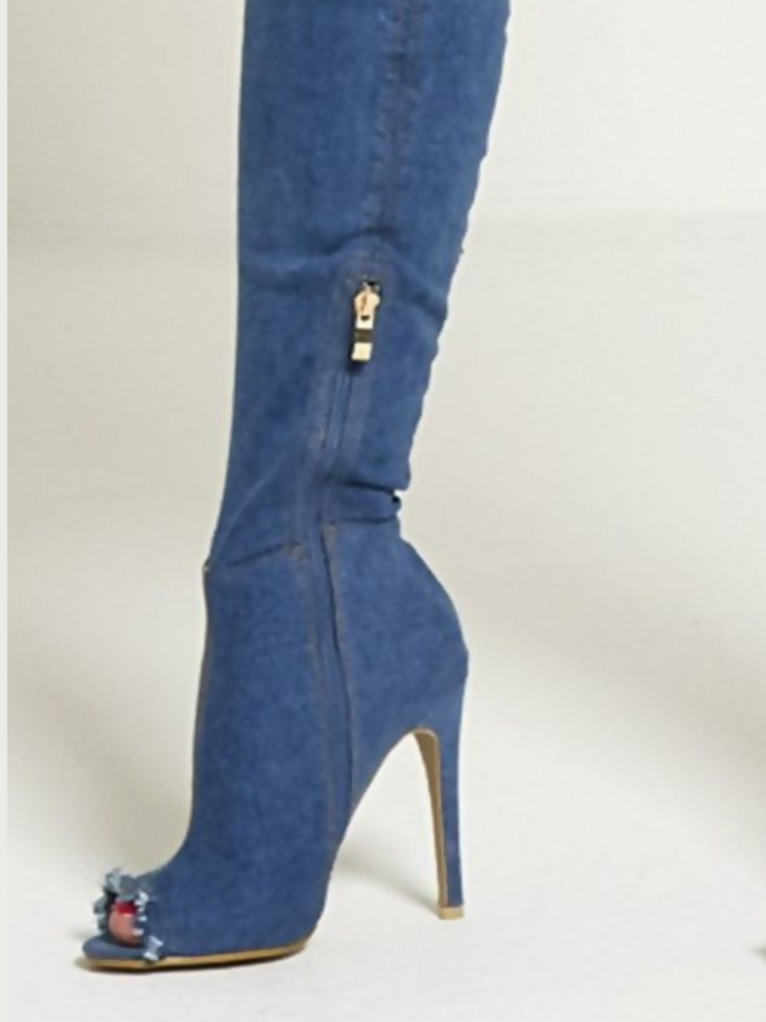 Close up of the inside of the dark denim thigh high boot with a peep toe shoe design. The boot shows a stiletto heel and inside zipe closure of the boot. The freyed peep shoe boot is also visible.