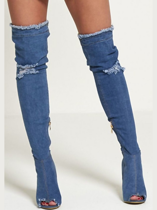 Model wears a dark denim thigh high boot that has a peep toe design and freyed edges and a distressed denim look. The boots has a stiletto heel and side zip fasteinf. The distressed denim boot has an over the knee desgn. The model faces forward, with both feet apart. The peep toe front of the boot can be seen. 