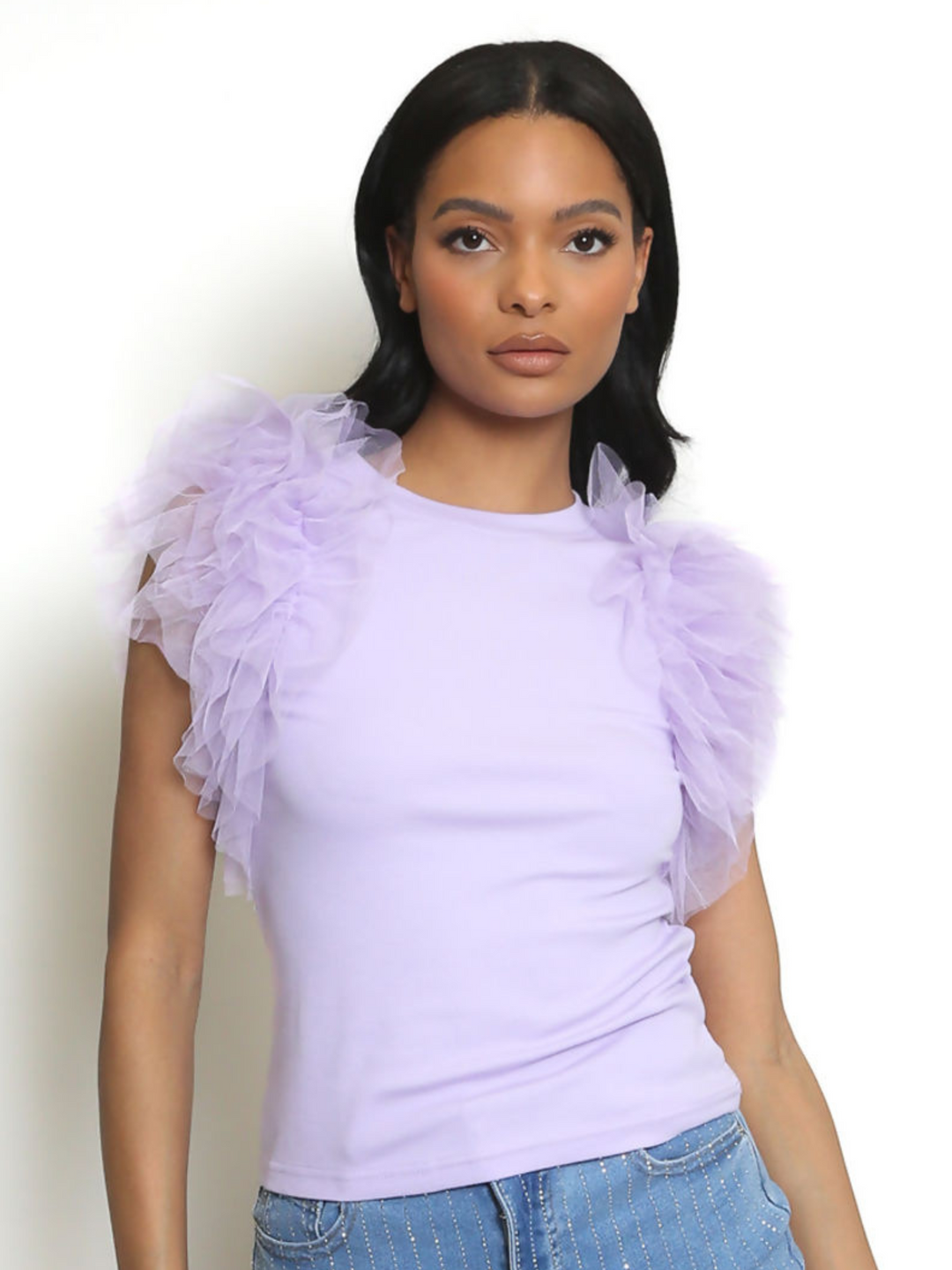Woman wearing a light purple top with ruffled sleeves against a white background. The lilac t shirt has a rounded neck and the frill organza sleeves are short. The model has light brown skin and long black hair, she faces forward, looking directly into the camera with her hands by her sides. 