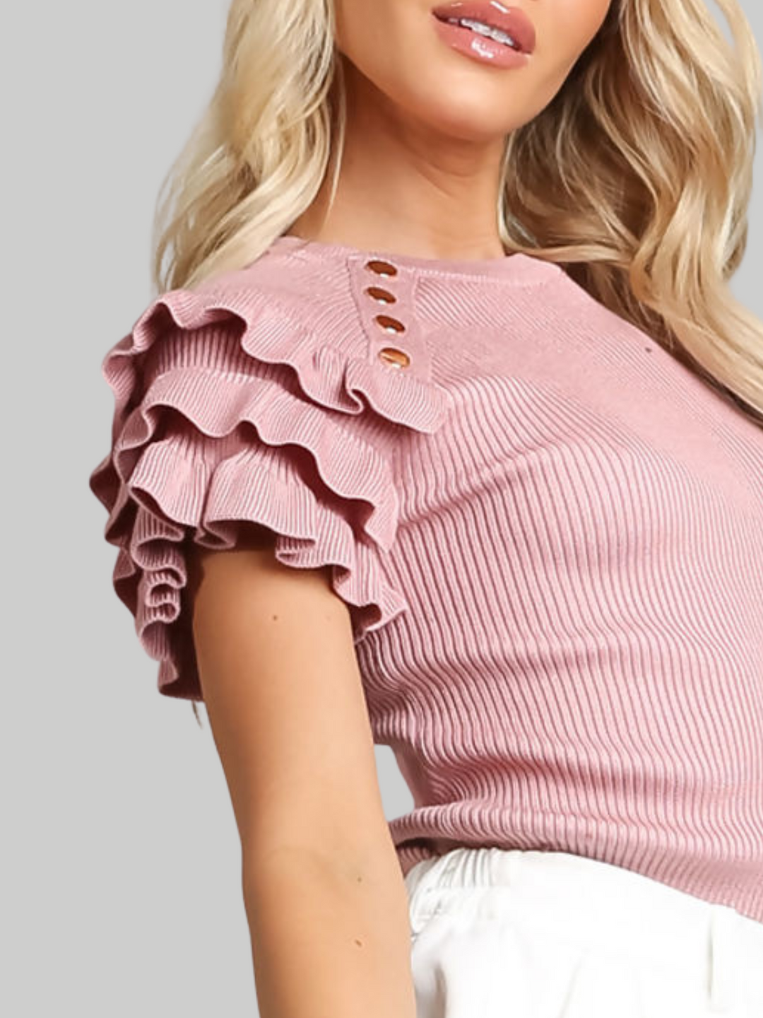 Close up of frilled sleeve. Female model wears a pink ribbed top with ruffled 3/4 length top and and gold buttons detailing. 