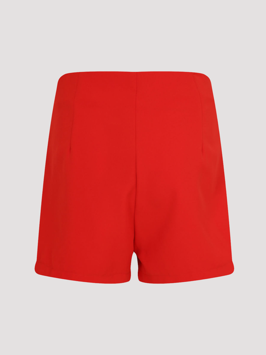 Ghost manequin stands in front of a plain background. The ghost mannequin wears a tailored red shorts, with front gold button trim. The ghost mannequin stands with its back to the camera, the back of the red tailored shorts can be seen, including the red plain design. 