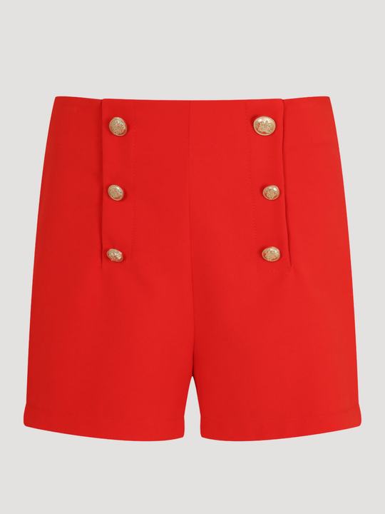 Ghost manequin stands in front of a plain background. The ghost mannequin wears a tailored red shorts, with front gold button trim. The ghost mannequin faces forward, the front of the gold button can be seen. 