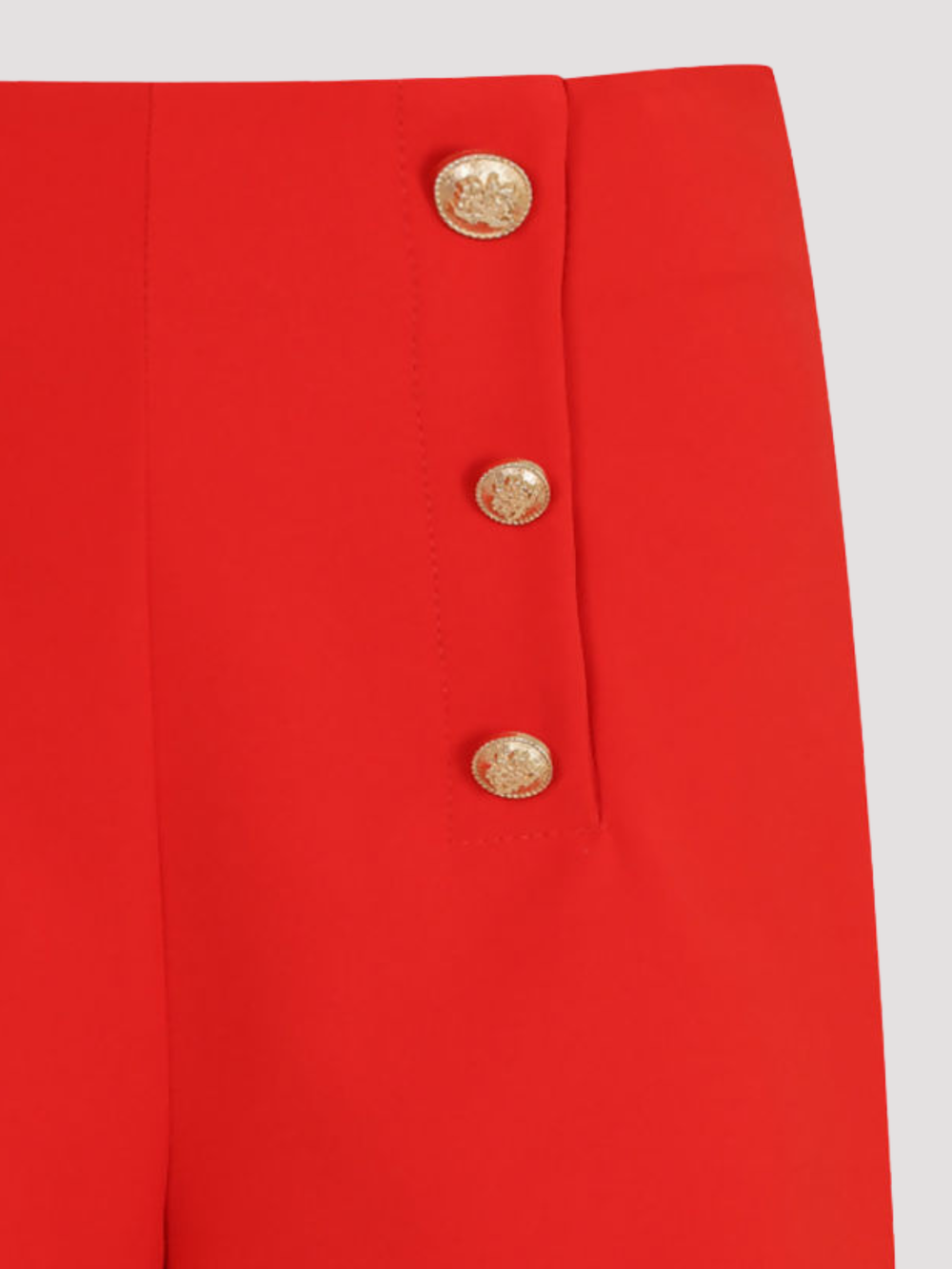 Close up. Ghost mannequin wears a tailored red shorts, with front gold button trim. A close up of the front gold button detailing can be seen. 