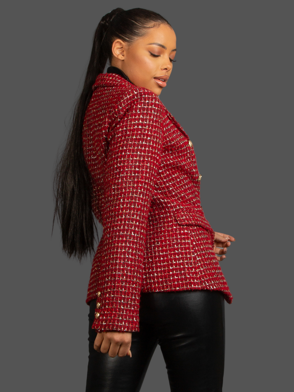 Model wears Red Wine Double Breasted Tweed Blazer, With Metallic Yarn Shimmer and Military Gold Buttons. The model as light brown skin and her hair pulled back into a ponytail. The model turns to the side and looks down, the back and side of the blazer can be seen. 