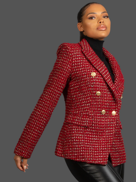 Model wears Red Wine Double Breasted Tweed Blazer, With Metallic Yarn Shimmer and Military Gold Buttons. The model as light brown skin and her hair pulled back into a ponytail. The model stands to the side and tilts her head upwards slightly, looking into the camera, she has one arm out stretched; the front and side of the blazer can be seen, including the gold buttons. 