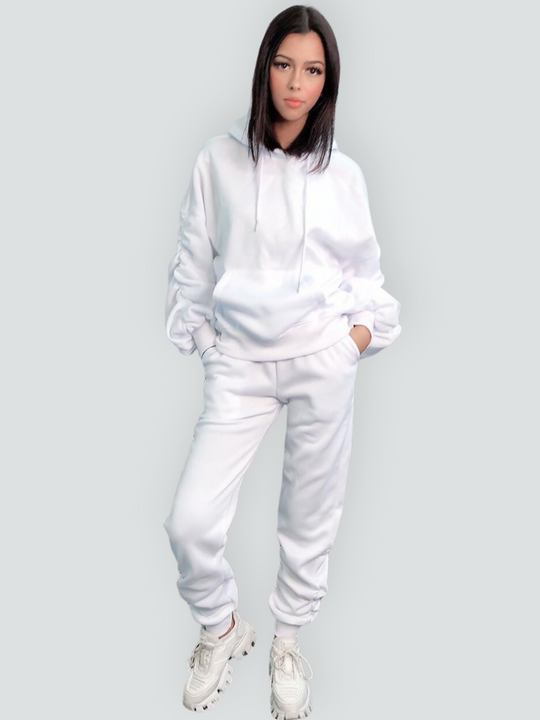 Full lenghth shot. Model wears a ruched sleeve hooded jumper which has an adjustable hooded draw string  tightening if required. The hood comes with a matching white joggers that has a ruched design at the ankles. The model stands to the side, she turns her head slightly to face the camera and slightly tilts her head. Model stands facing the camera with both hands in the jogger pocket. She faces directly into the camera.