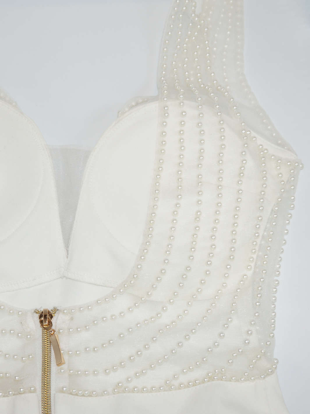Close up of the cream premium deluxe low back pearl dress with gold chunky zip fastening to the rear. The pearl detailing and gold chunky zip fastening can be seen in the photograph. The pearls are stiched onto a clear meshed material.  