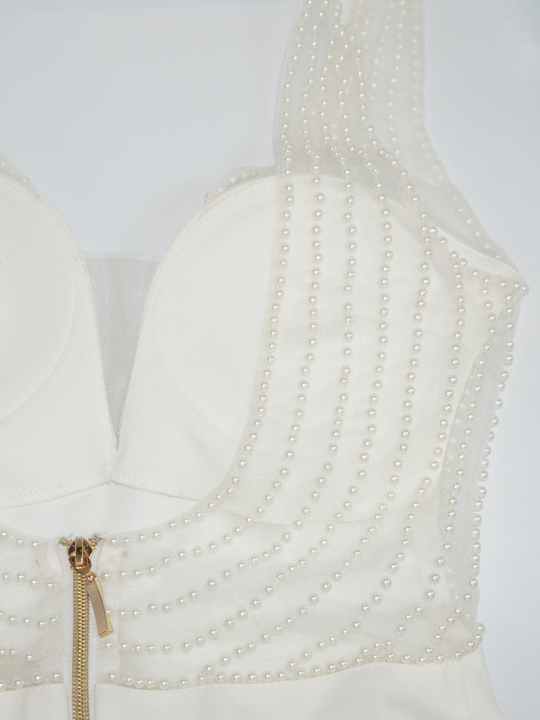 Close up of the cream premium deluxe low back pearl dress with gold chunky zip fastening to the rear. The pearl detailing and gold chunky zip fastening can be seen in the photograph. The pearls are stiched onto a clear meshed material.  