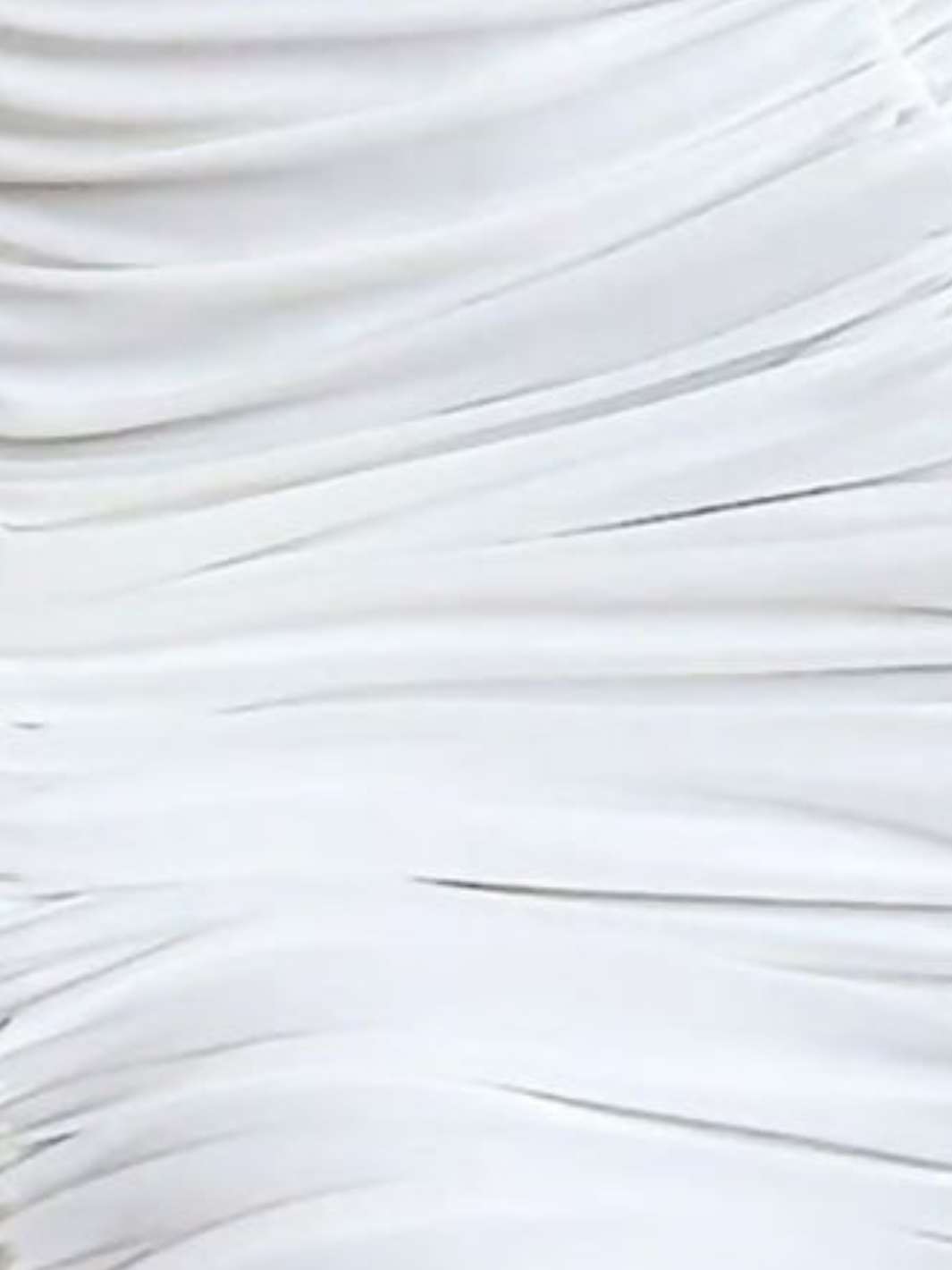 Closeup of the slinky ruched material. The dress has double lined slinky white ruched midid dress with draping detailing at the torso
