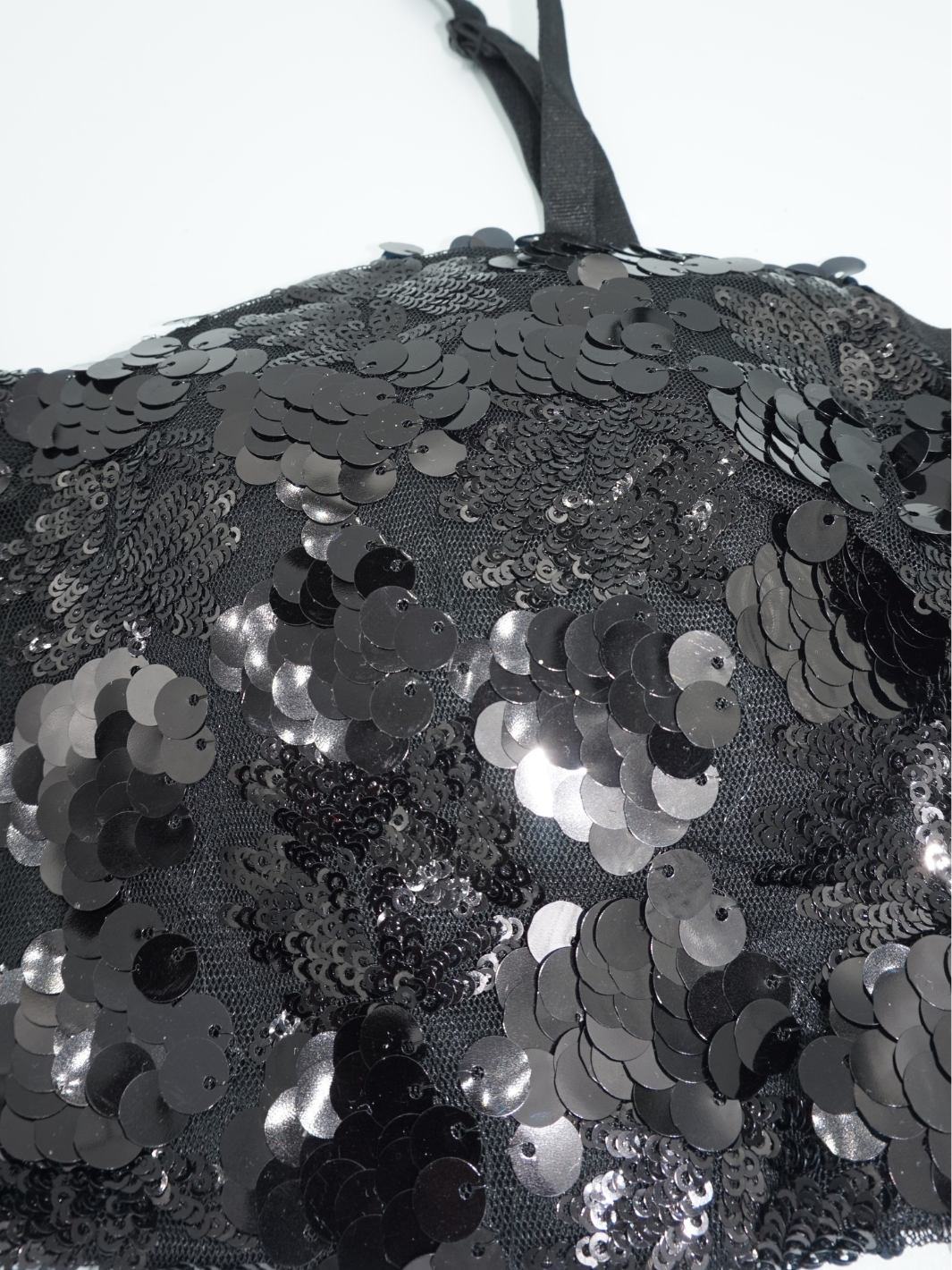 Flat lay photo of the  black sequin brallette with spaghetti straps.  The closeup demionstrtaes the black sequin detailing. 