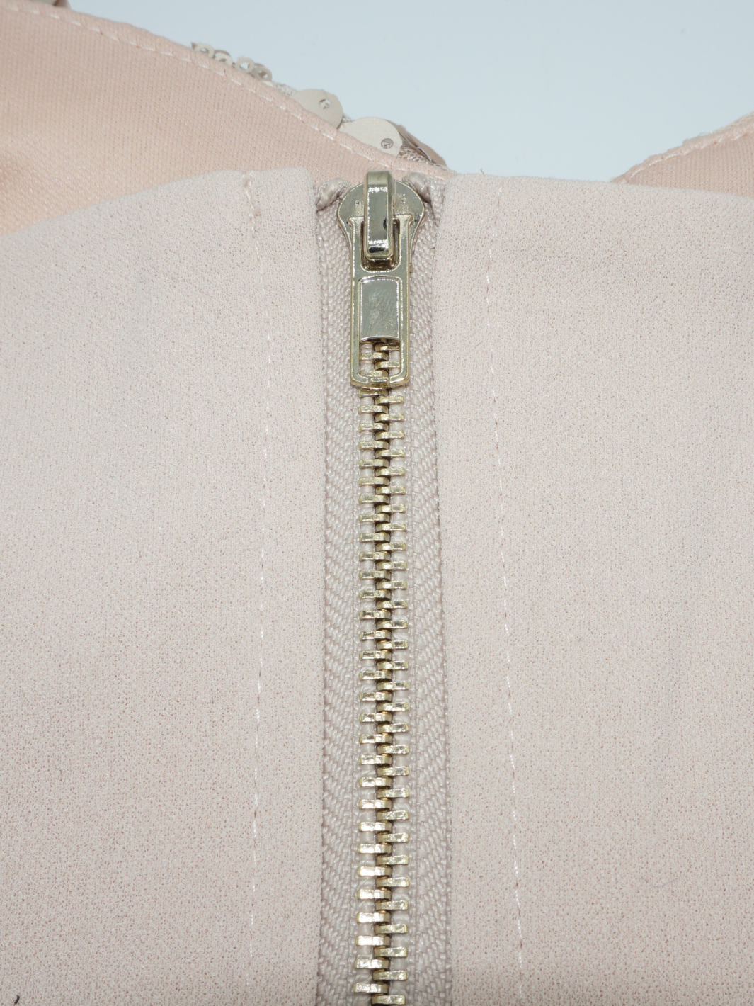 Closeup of the chunky gold zip fastening that is positioned to the rear of the bralette. 