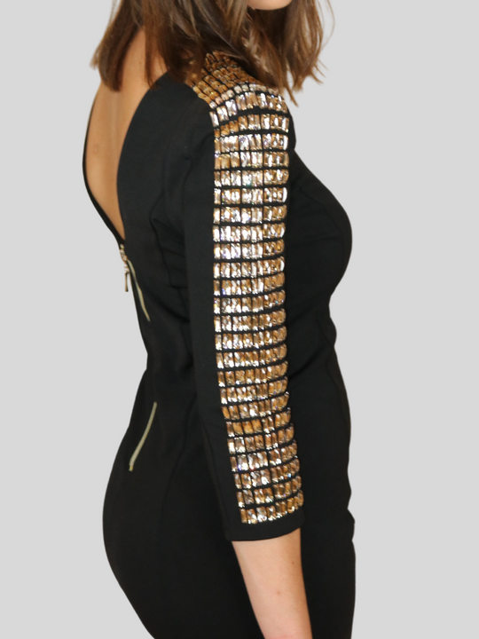 4ever Stunning Deluxe Premium black midi dress with gold rhinestone jeweled arms and chunky gold back zip fastening. Model stands to the side, the rhinestone sleeved arms and the chunky  zip fastening is visible.