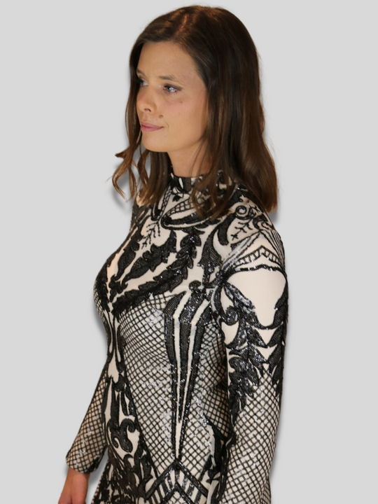 Model wears 4ever stunning premium deluxe a sequined  cream and black long sleeved dress, with a high neck and chunky gold back zip fastening.  Model looks to the side, the sequined sleeve and front of the dress is  visible. 