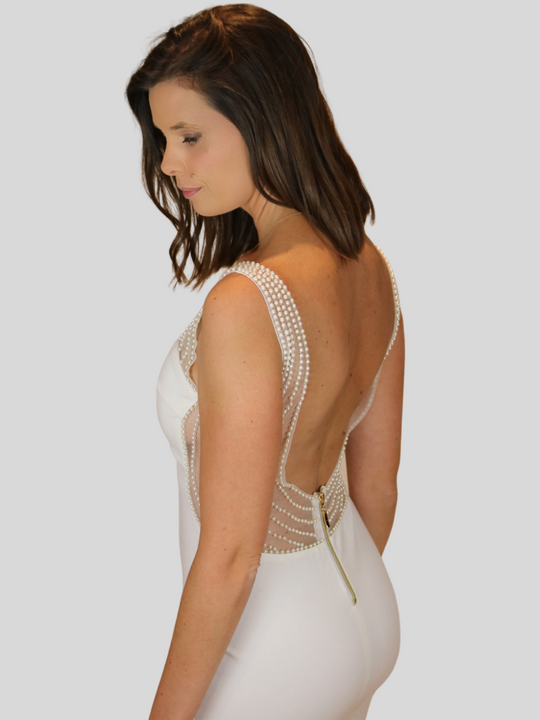 Model wears the white version of the Premium Deluxe low back pearl dress. Model looks down and stands to the side. The side and back of the dress can be visible. The low back plunging dress is visible.
