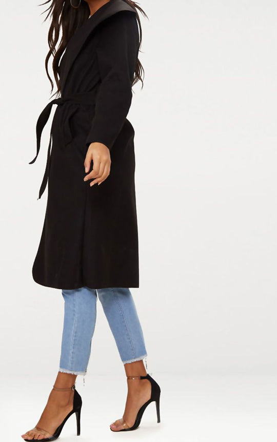 Black long duster coat with complimentary belt. Model stands to the side.