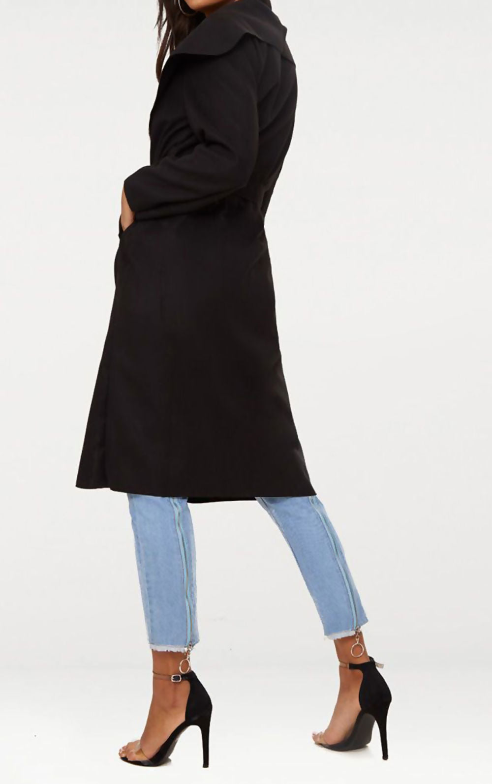Black long duster coat with complimentary belt. Model stands with her back to the camera showing the side of the coat.