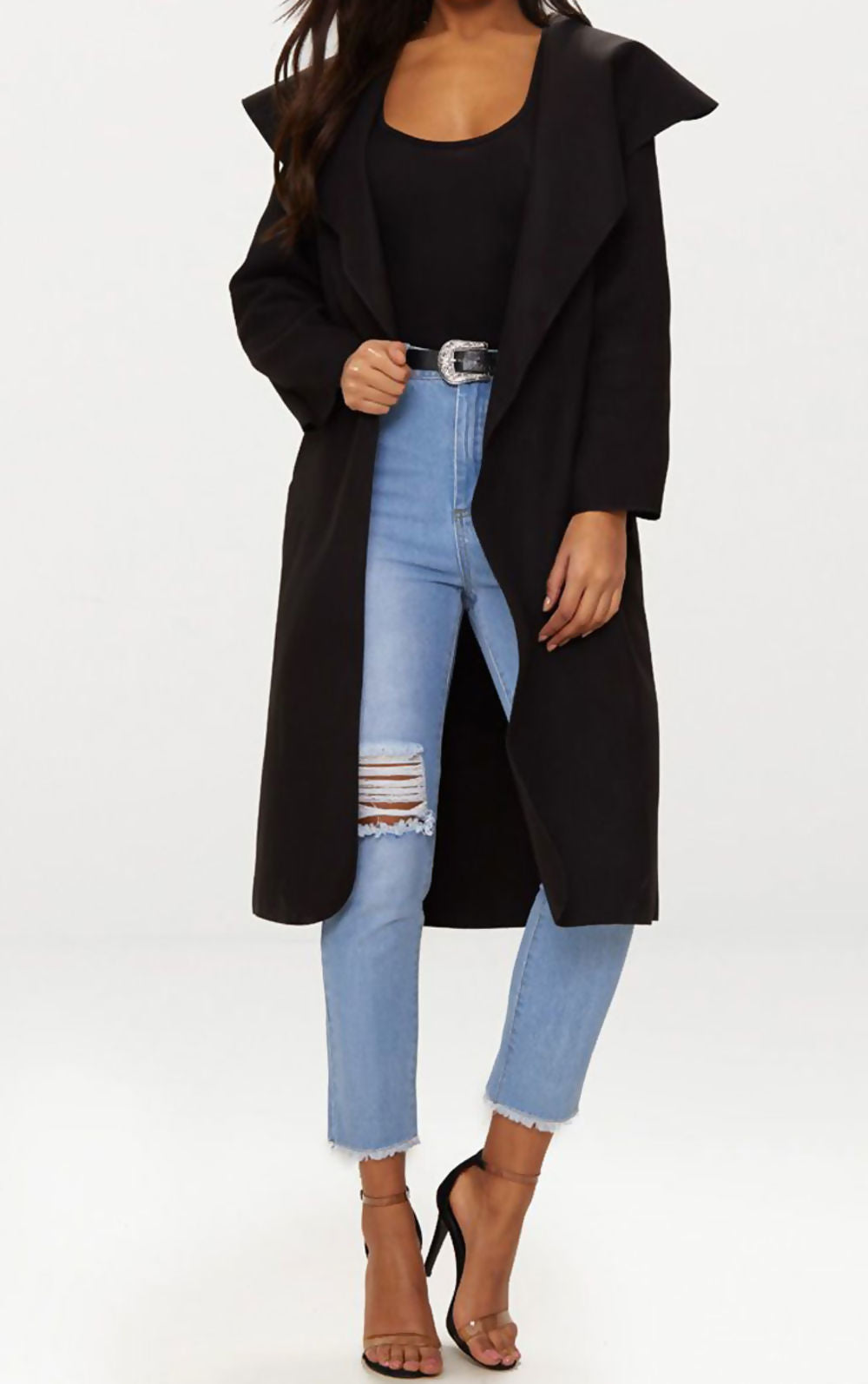 Black long duster coat with complimentary belt. Model faces forward with the duster coat open. Model holds onto one side of the duster coat.
