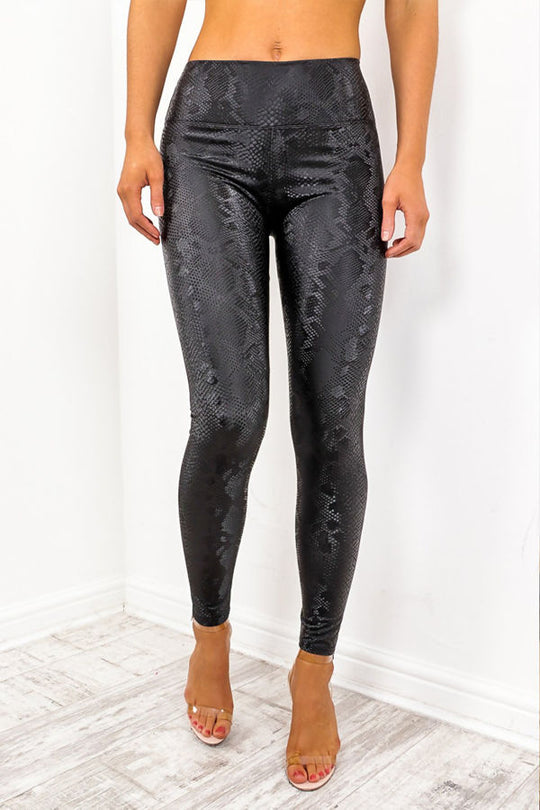 Model wears snake skin leggings with high waisted panelling. The snake skin pattern is visible.  Model faces the camera with legs slightly apart and one leg slightly behind the other.