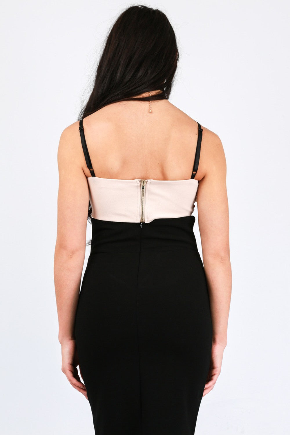 Model wears pink sequined bralette with thin black strap and chunky back zip fastening.  Model has her back to the camera, the chunky zip fastening is visible. Model pairs the bralette with a long black pencil skirt. 