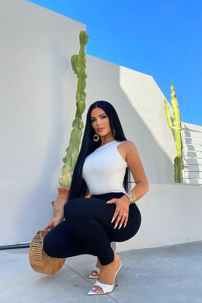 Model wears cream slinky double layered bodysuit. Model kneels down, holding a basket bag in one hand. 