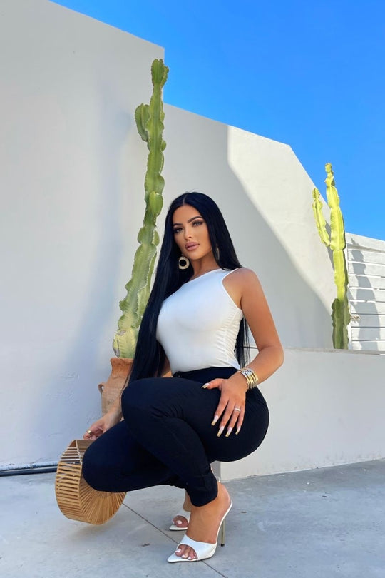 Model wears cream slinky double layered bodysuit. Model kneels down, holding a basket bag in one hand. 
