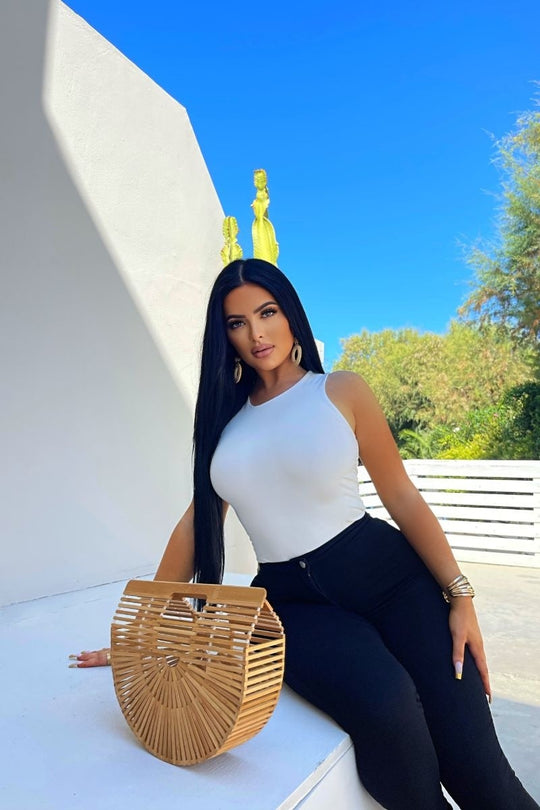 Model wears cream slinky double layered bodysuit. Model is outside and sits on a white bench. 