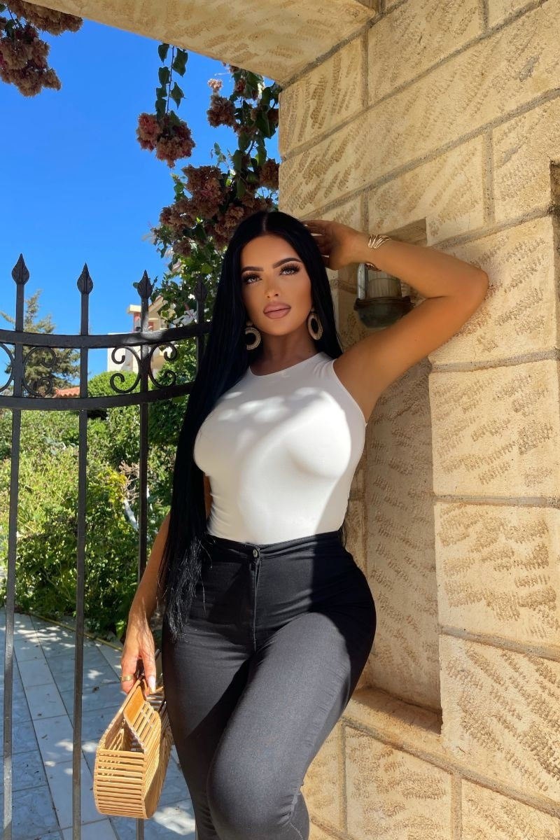 Model wears cream slinky double layered bodysuit. Model ia outside and places her hand on her head.