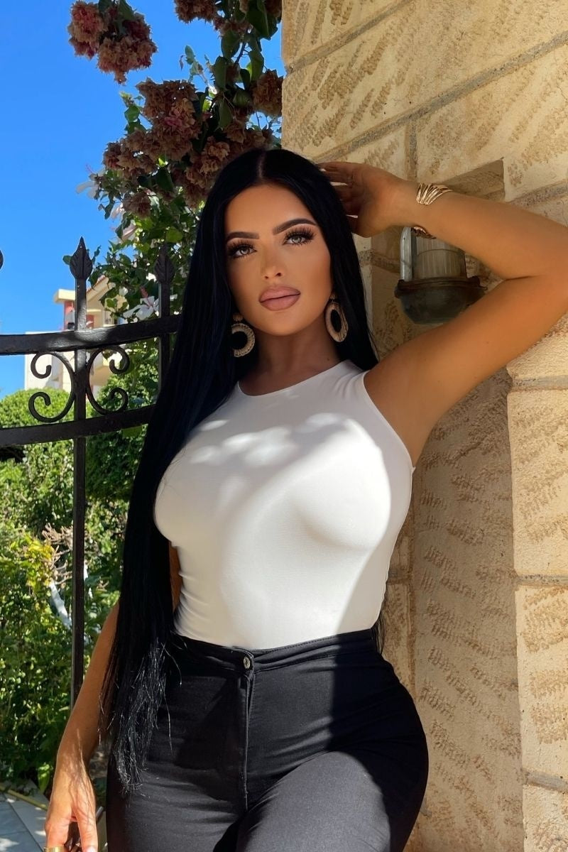 Model wears cream slinky double layered bodysuit. Model places one hand on her head.