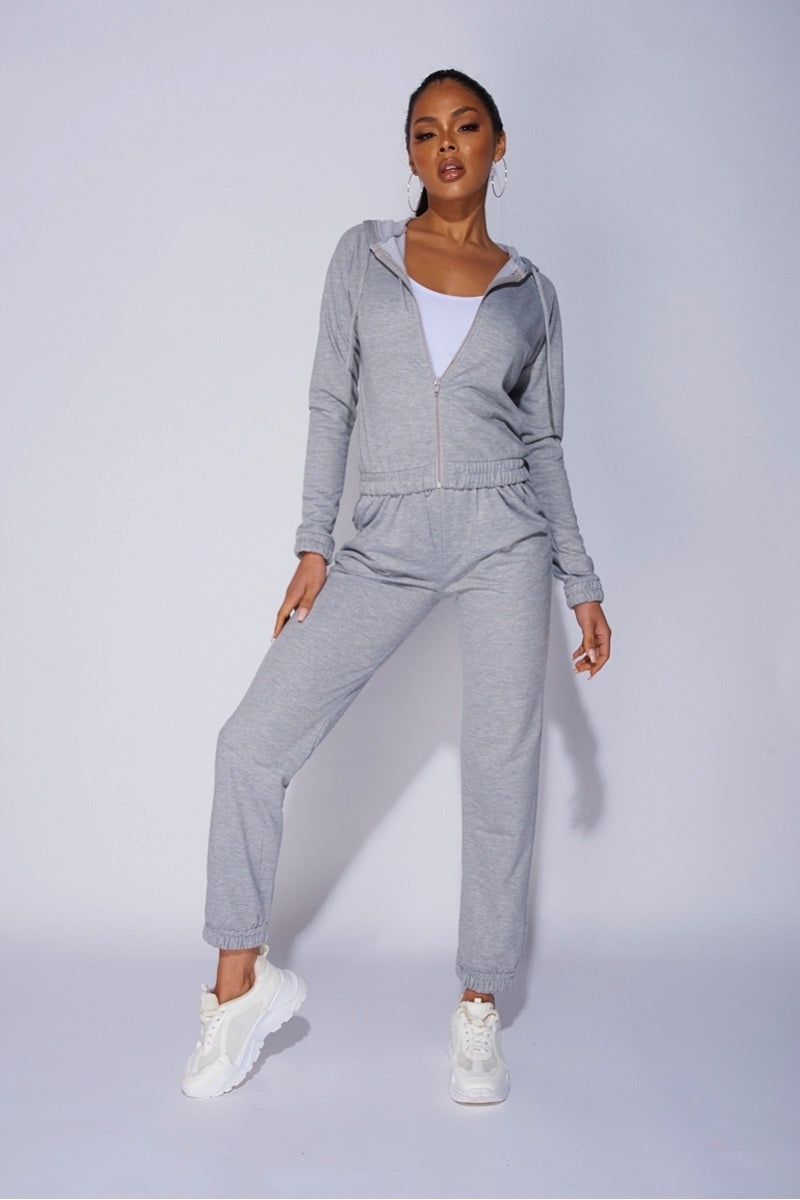 Model wears a light weight tracksuit with front zip fastening and draws string hood.  Model places one leg to the side and looks directly into the camera.