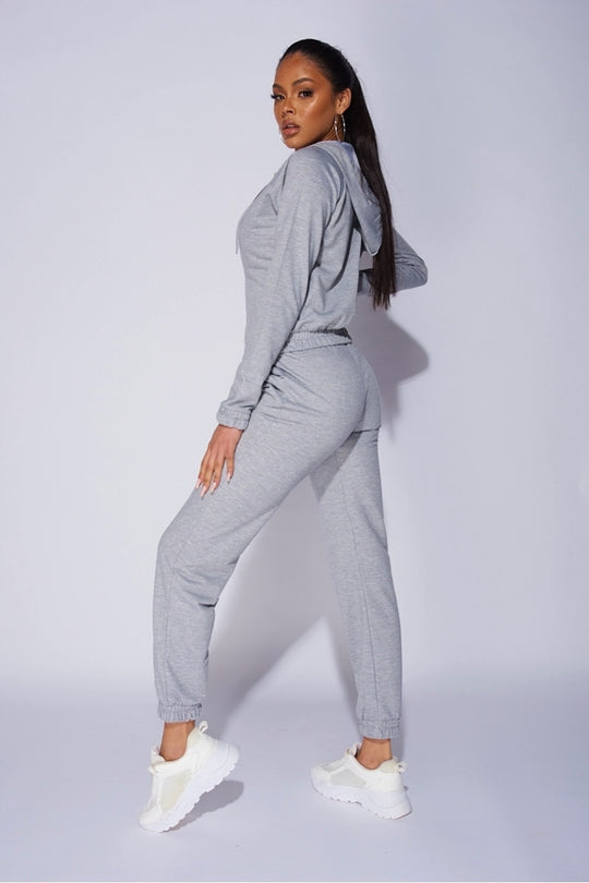 Model wears a light weight tracksuit with front zip fastening and draws string hood. Model stands to the side, placing one leg in front of the other. Model turns her head so that she is looking directly into the camera. 