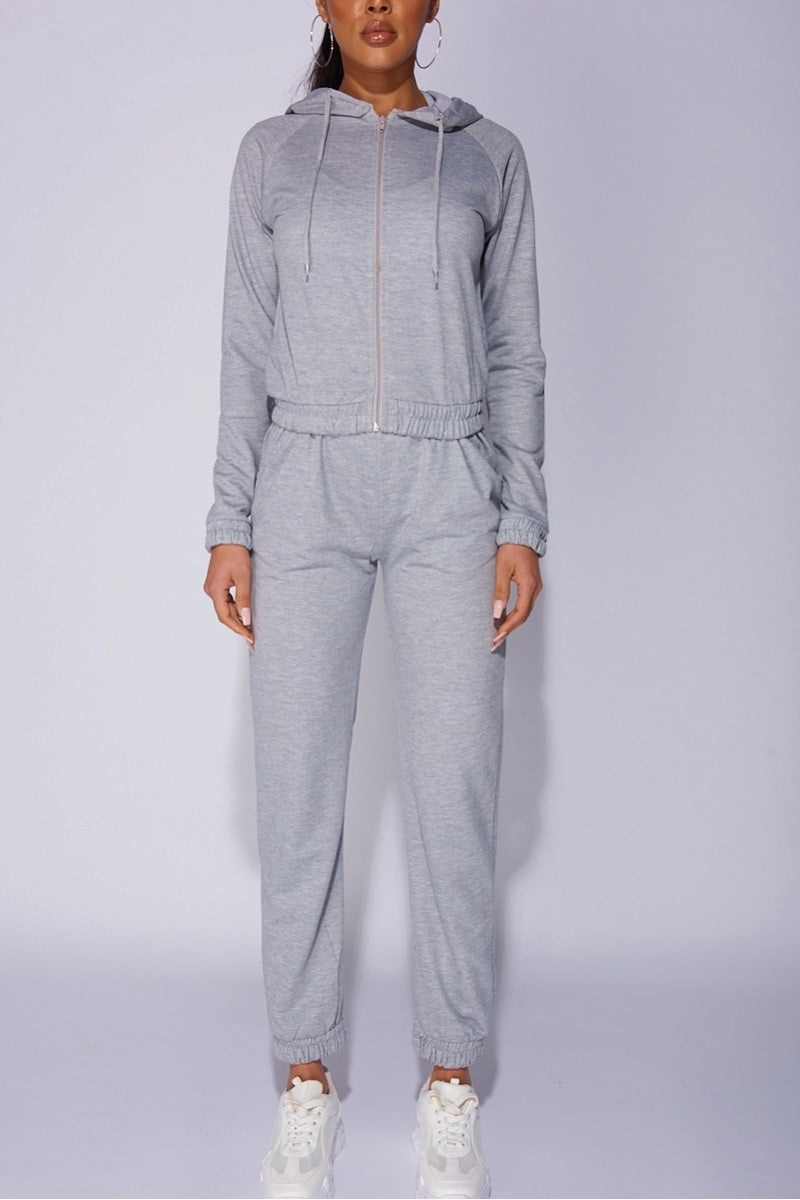 Model wears a light weight tracksuit with front zip fastening and draws string hood. Model stands directly facing the camera, with legs slightly apart and hands  by her sides.